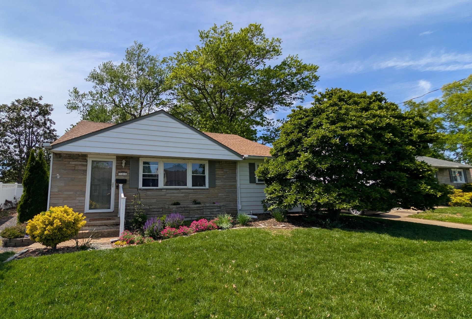 Front of the house in May 2026. Full beds, flowers in bloom, established plantings.
